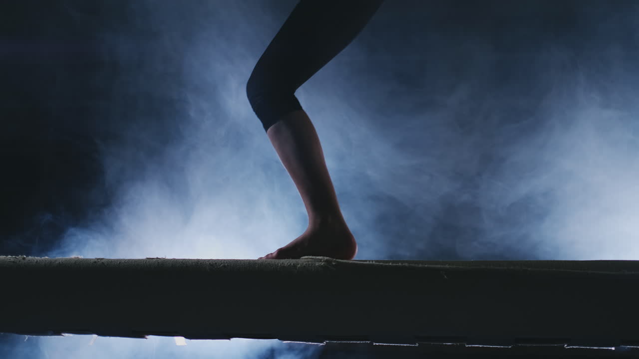 Legs Professional girl gymnasts jump in slow motion in the smoke on the balance beam. Women's Artistic Gymnastics