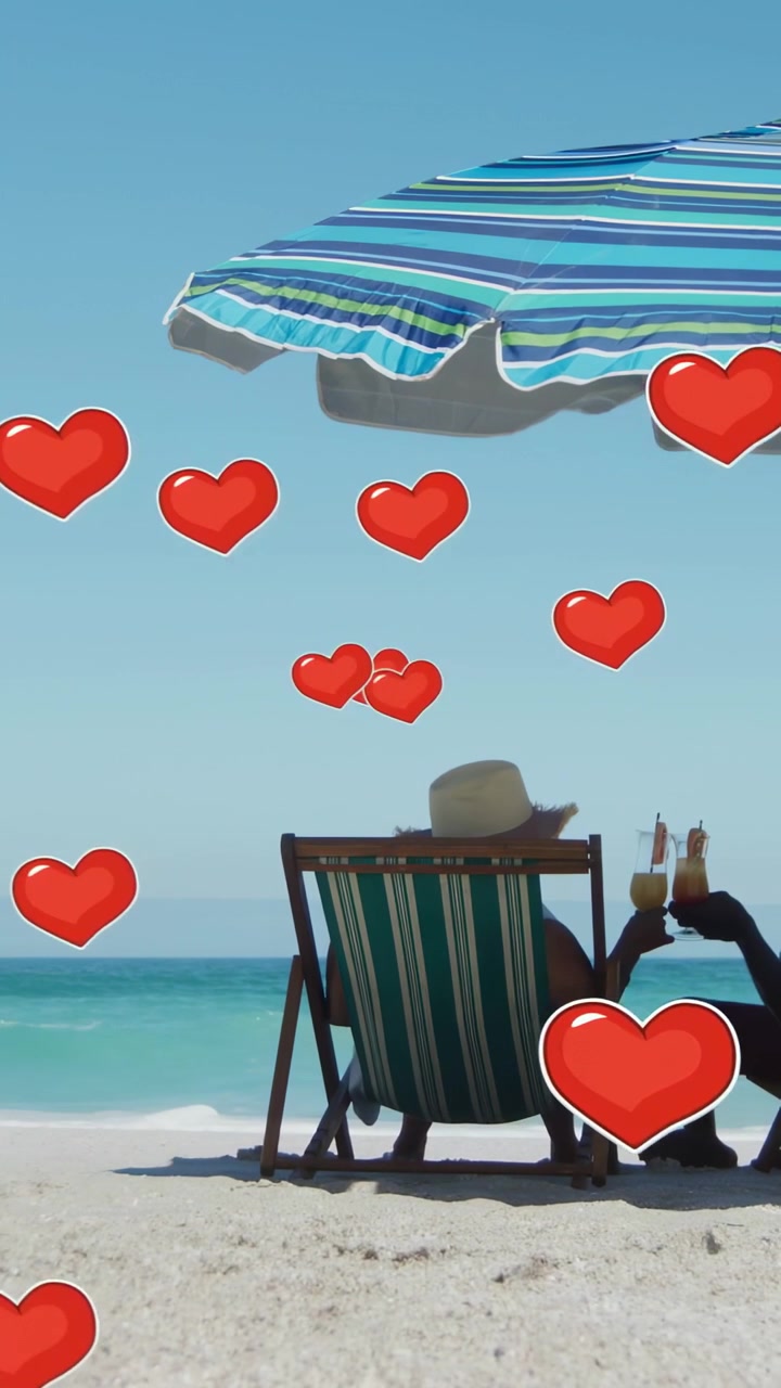 Vídeo vertical: Homem levantando a bebida para a mulher na praia, brindando, corações flutuando em torno de uma viagem romântica.
