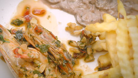 meat in sauce, prawns, steamed vegetables and french fries, close-up, mediterranean