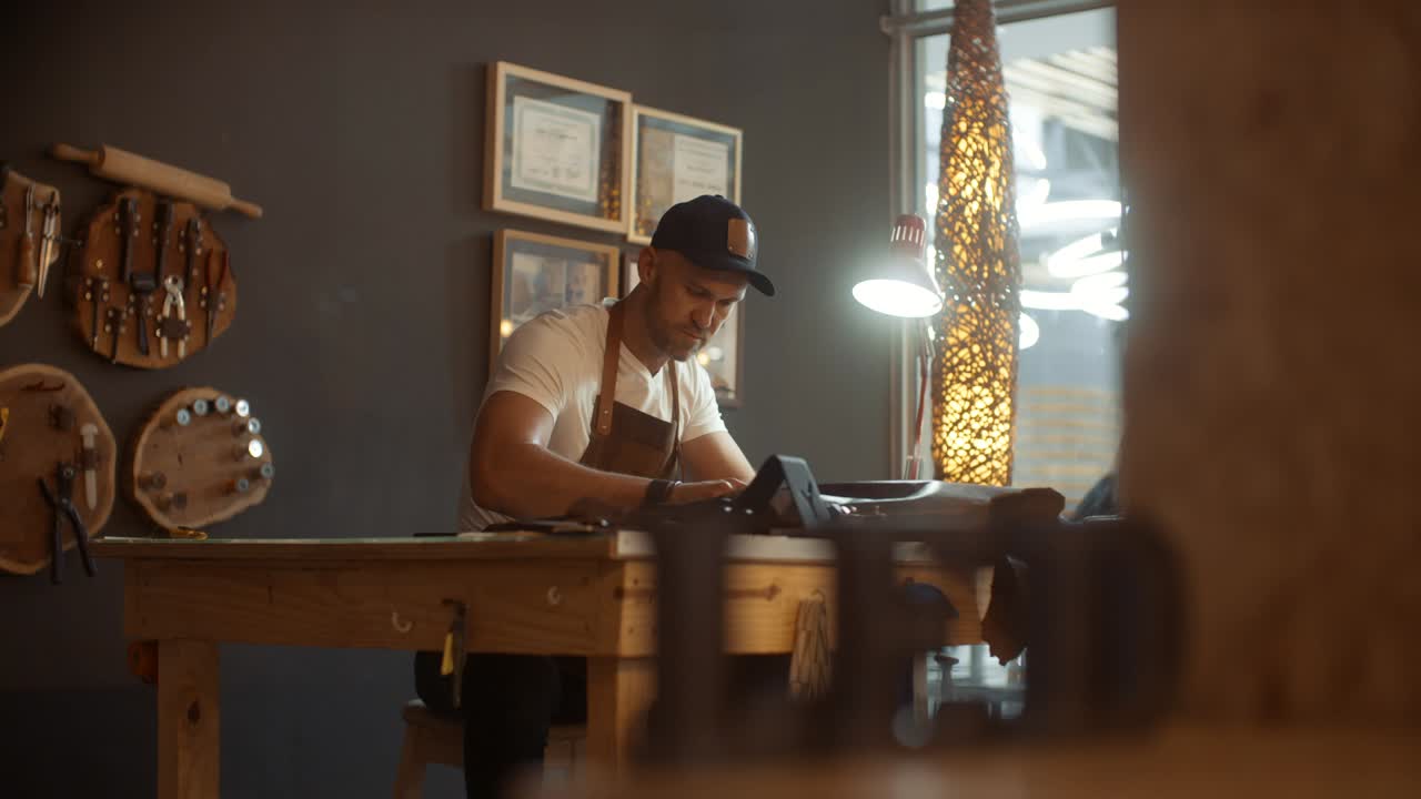 Artisan working in his retail shop with tools hanging on the wall behind him as focus of camera is racked from the letters LED to the artisan