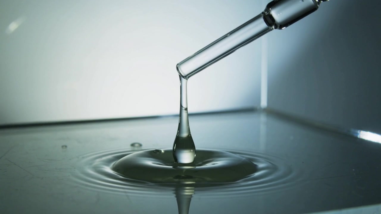 Dripping glass pipette forming viscous column on lab tabletop, creating ripples for fluid study