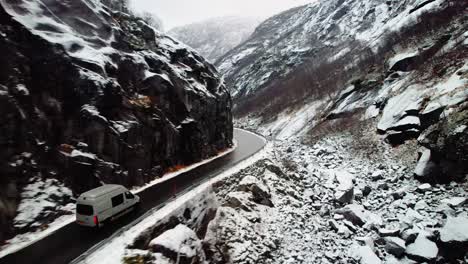 un campista conduce a través de un camino nevado y sinuoso entre montañas rocosas en noruega