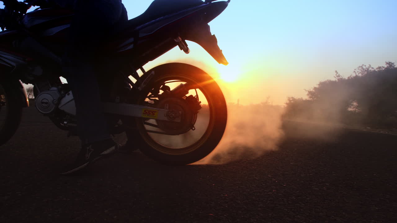 Sunset burnout, silhouette of the back of a motorcycle as it creates a cloud of dust while doing a burnout with a golden sunset in the background.