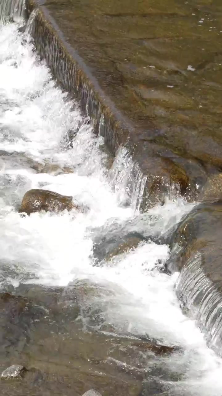 Un'inquadratura dall'alto cattura l'acqua fresca del fiume che scende a cascata su gradini di pietra in piena luce diurna