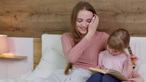 madre joven y hijo niña hija acostada en la cama en casa, leyendo libros cuentos para dormir, cuentos de hadas