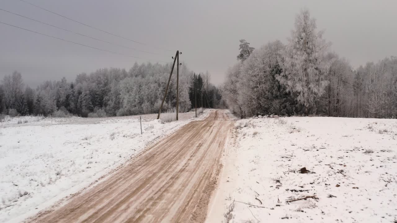 Flying fast over a sandy gravel road in winter with lost of snow and frost on trees. Driving in countryside on a winter day. Aerial drone shot in winter.