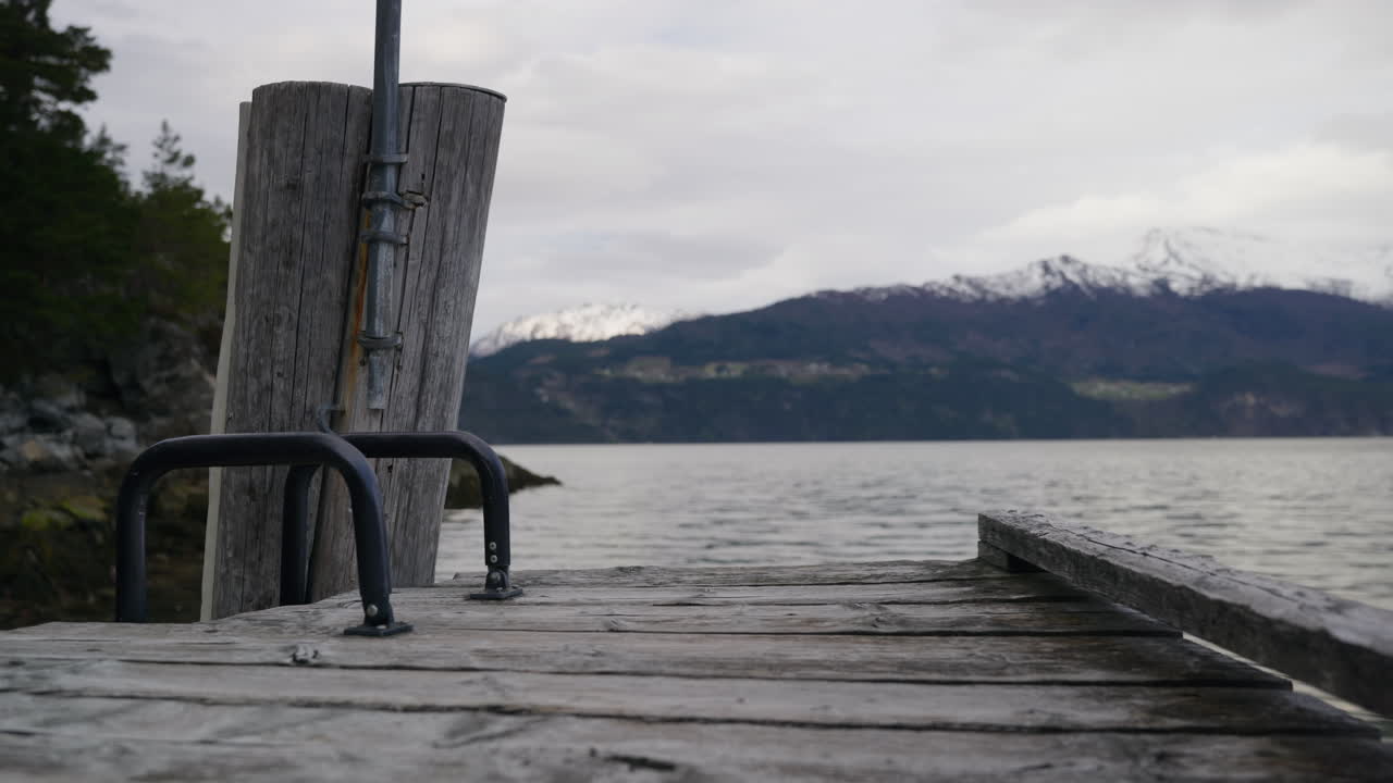 A rustic wooden pier stretches out towards calm waters, framed by snow-capped mountains in the distance. Perfect for travel features or serene landscape projects
