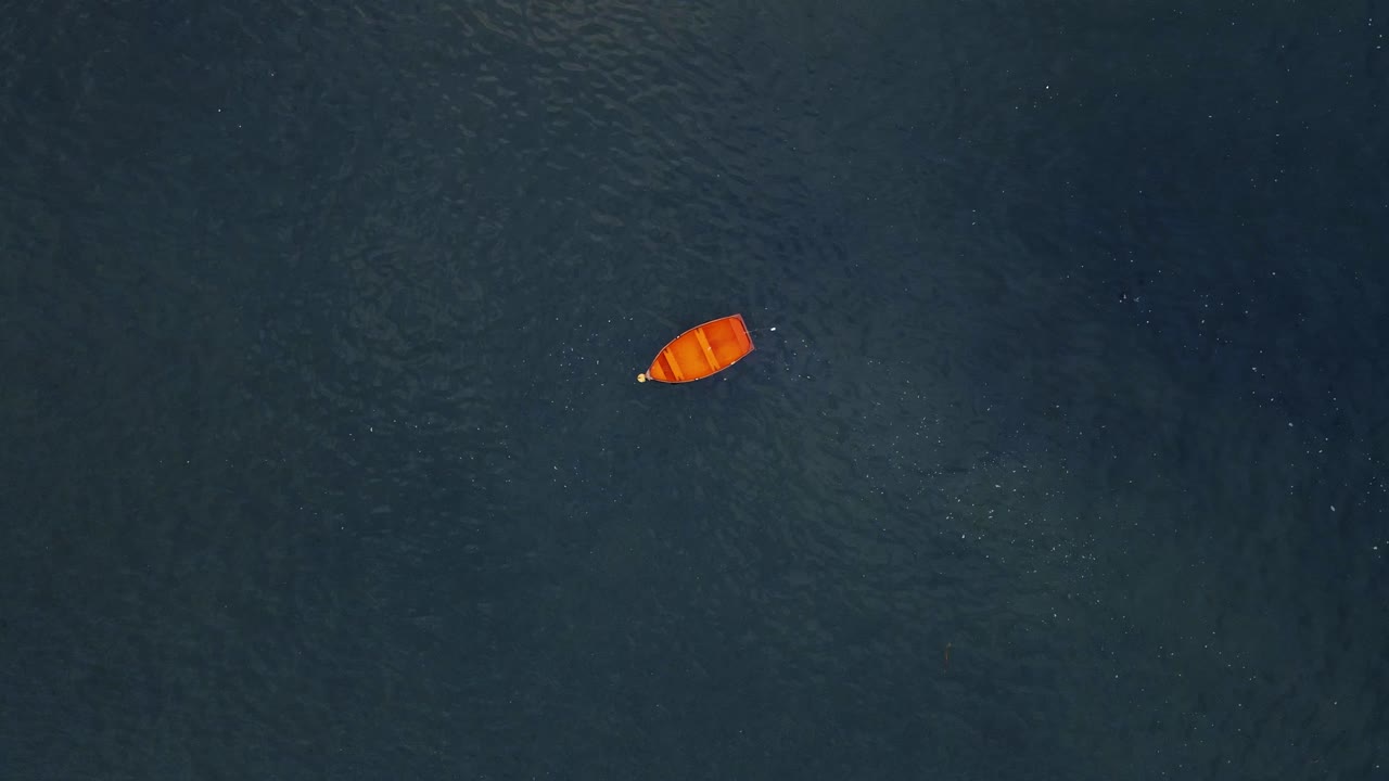 Drone shot above small red wooden boat tracking and spinning towards it with vast open water around the boat