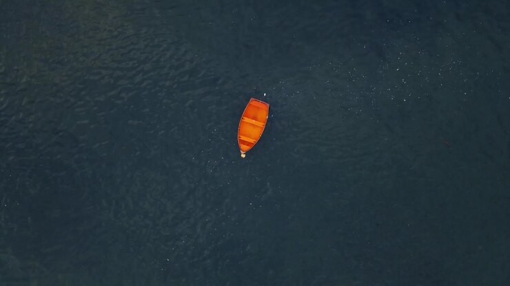 Drone shot above small red wooden boat tracking and spinning towards it with vast open water around the boat