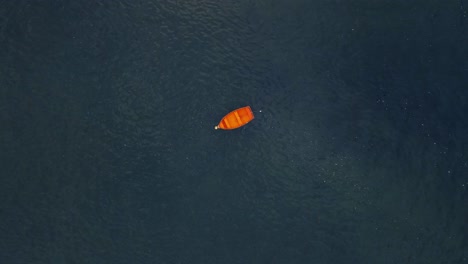 Drone-shot-above-small-red-wooden-boat-tracking-and-spinning-towards-it-with-vast-open-water-around-the-boat