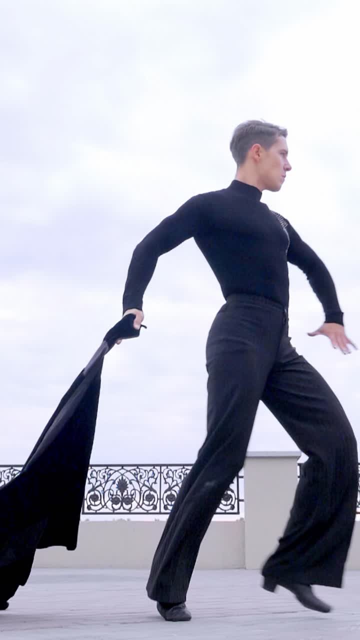 Male dancer in black attire performing dynamic movements on an outdoor stage with elegant backdrop