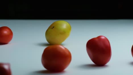 heirloom and cherry tomato rolling on the white table surface in slow motion reverse