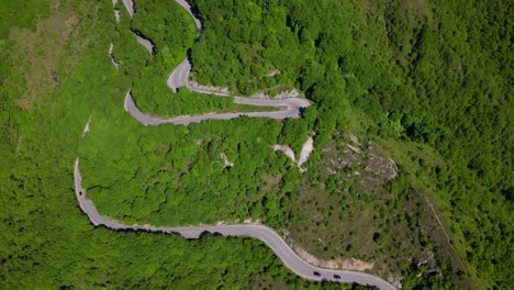 wide top-down aerial shot of multiple switchbacks cutting through the forested mountain slope with sparse traffic. shot at selvino, italy (selvino, italia)