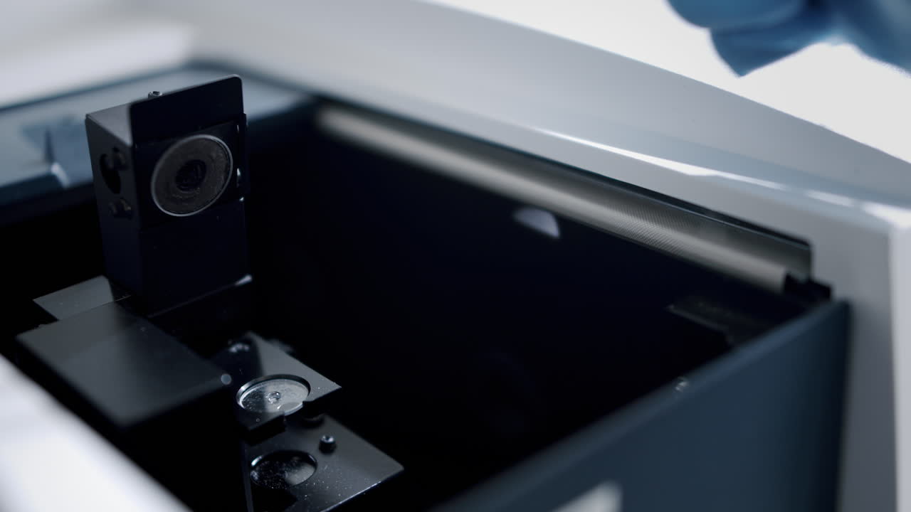 파란 장갑을 입은 과학자가 현미경 에 플을 넣고 있습니다.