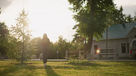 dama con ropa gris leyendo un libro mientras camina por el campo cubierto de hierba al aire libre, la luz del sol ilumina los alrededores, con una vista parcial de un coche estacionado y un edificio en el fondo