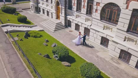 bride dances and hugs groom near dwelling building aerial