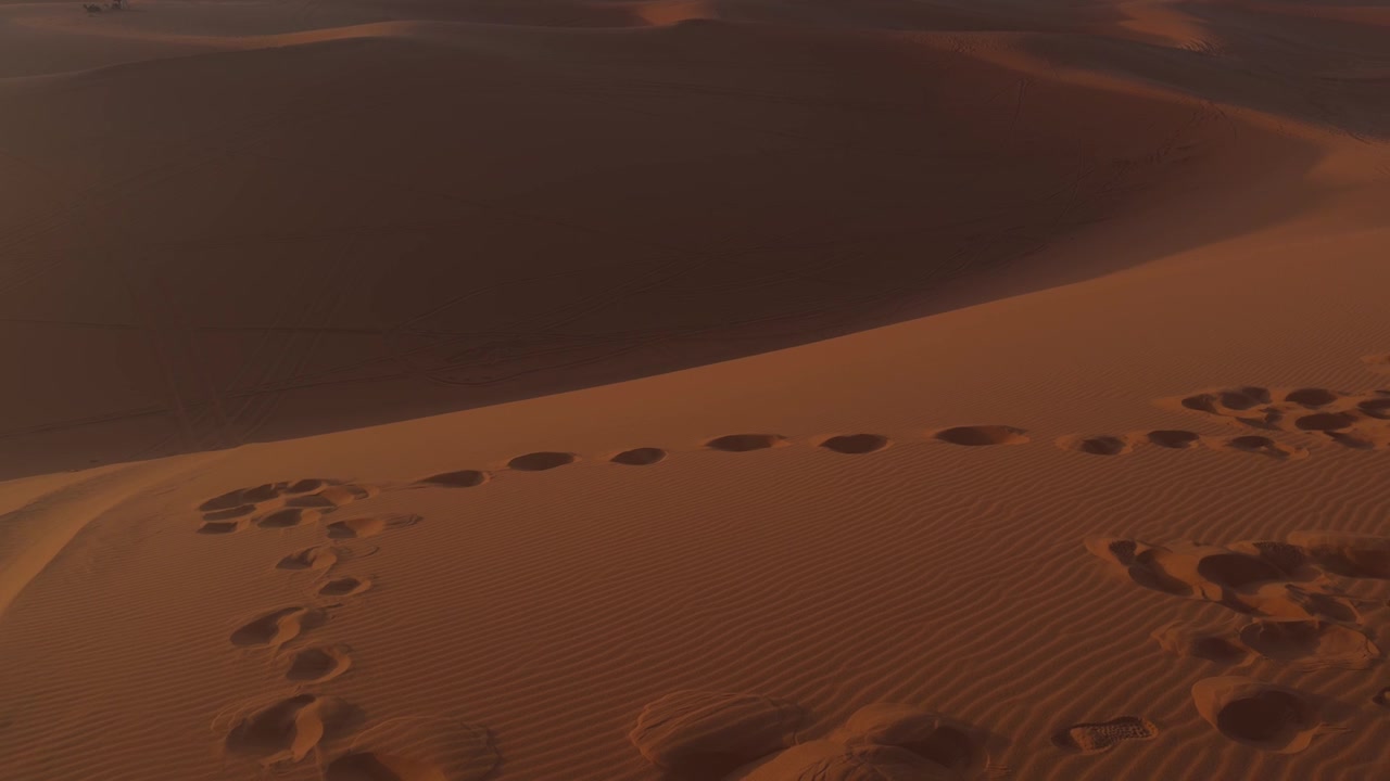 Impronte umane si snodano lungo la cresta curva di una duna di sabbia arancione del Sahara alla luce dorata.
