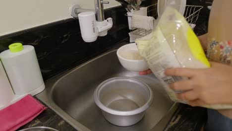 person measuring rice grains with small bowl before pouring into cooker in the sink