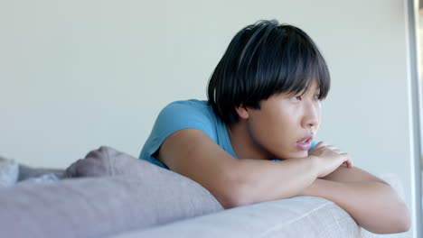 asian college student lying on couch, looking thoughtful