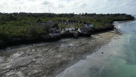 Kisini-Beach-bungalow-resort-at-low-tide-in-East-Zanzibar-Island-Tanzania-Africa,-Aerial-approach-shot