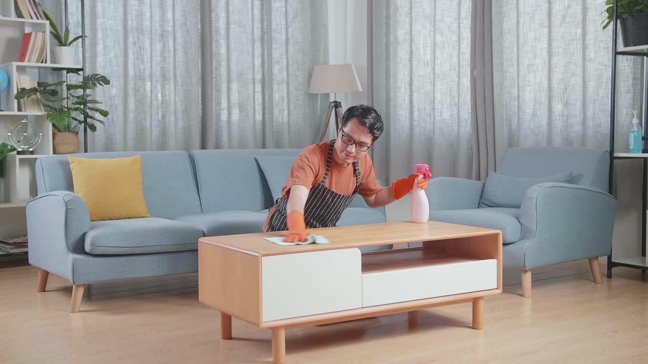집에서 스프레이로 테이블을 청소하는 아프론을 입은 아시아 남성 집주인