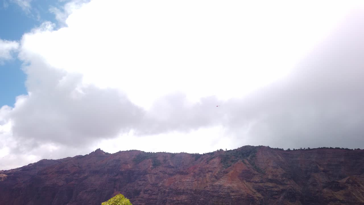 Gimbal wide follow shot of helicopters flying over Waimea Canyon from the lookout trail on the island of Kaua'i in Hawai'i
