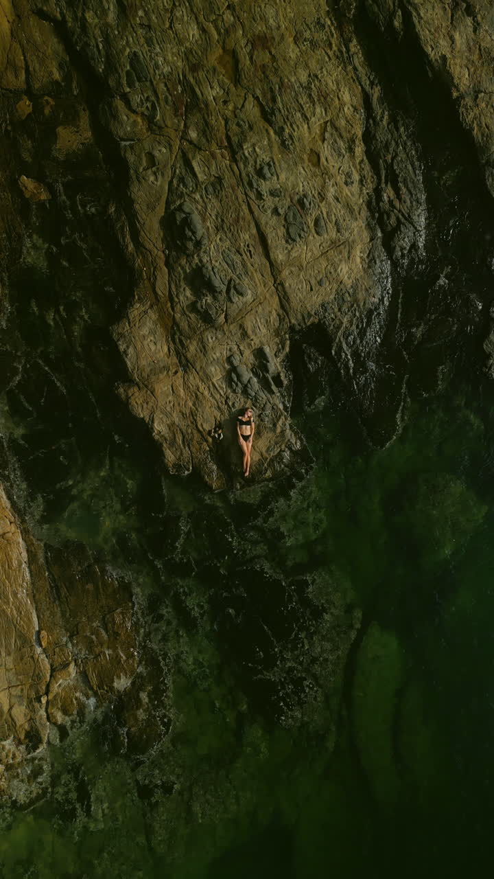 Mulher relaxando nas rochas junto ao mar