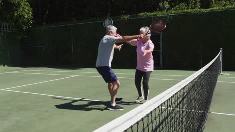 happy caucasian senior couple embracing on outdoor tennis court in sun after playing a game