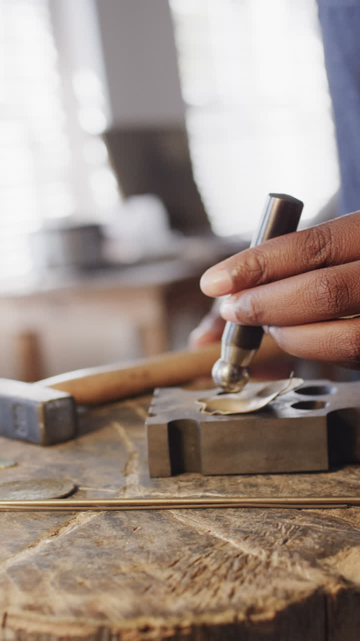 Vertical video of biracial female worker shaping ring with hammer in workshop in slow motion