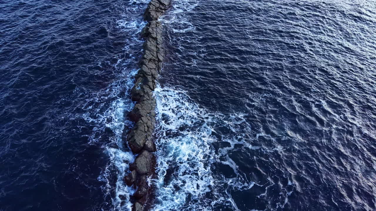 Un sentiero roccioso si estende attraverso acque di un blu profondo, collegando la terra all'oceano sotto un cielo sereno al tramonto.