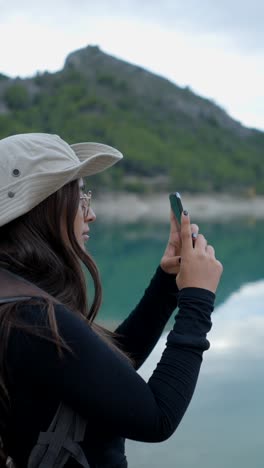 woman taking a photo of a scenic mountain lake with her smartphone