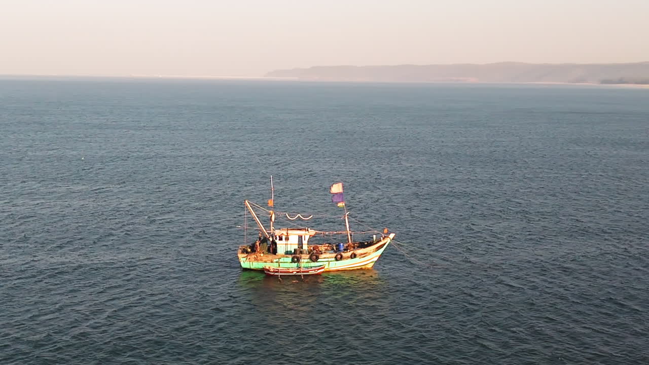 Aerial view around a traditional fishing boat in calm sea, golden hour in India