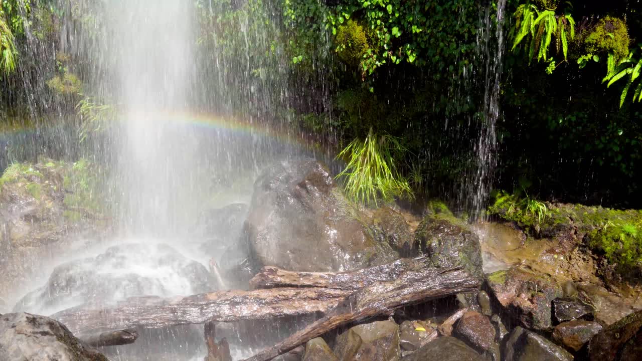 Salto La Niña Encantada waterfall spraying water over rocks forming a rainbow, surrounded by green rainforest in Liquiñe, Chile