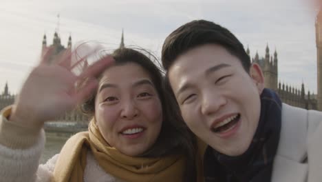 young asian couple on holiday making video call home on phone at houses of parliament in london uk 1