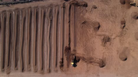 Static-aerial-shot-of-yellow-tractor-processing-compost-mixture-on-a-farm-in-mexico