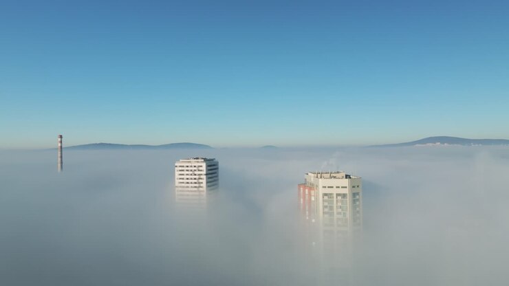 Vista aérea orbital de drone, banhada pelo sol, de arranha-céus imponentes perfurando nuvens de inversão brancas, revelando vistas da cidade e destacando a beleza cinematográfica da exploração urbana