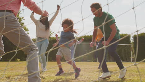 Enkel-Schießt-Als-Mehrgenerationenfamilie-Zu-Hause-Im-Garten-Ein-Tor-Und-Spielt-Fußball-Oder-Fußball