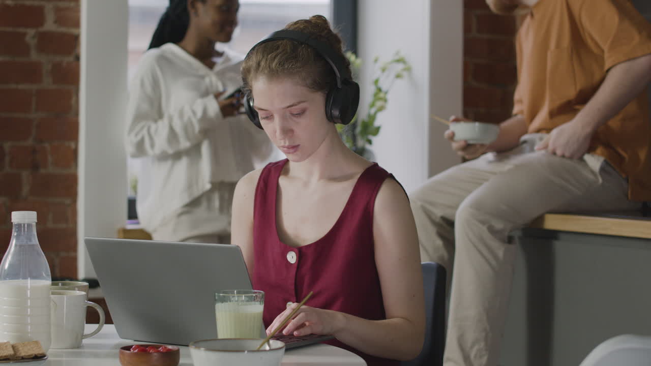 공유 아파트에서 랩톱 컴퓨터에서 작업하는 헤드폰을 가진 소녀