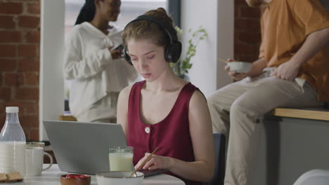 chica con auriculares trabajando en un ordenador portátil en un piso compartido
