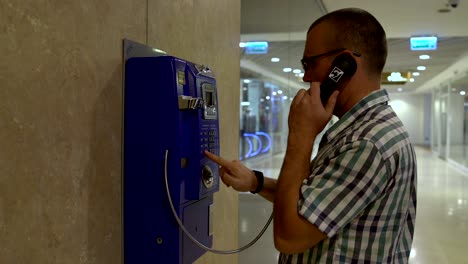 the man approaches the telephone and answers the phone and dials the number