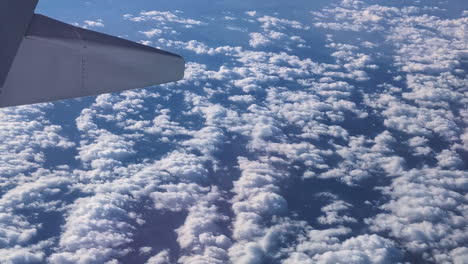 wig of an airplane flying above dispersed white clouds over blue skyline closeup