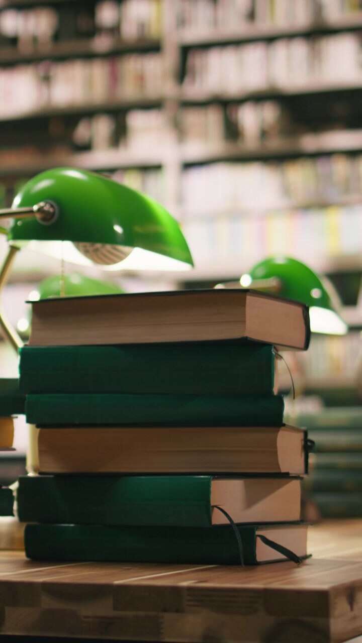 Video verticale: Pila di libri con copertina rigida su una scrivania di legno in una biblioteca universitaria vuota.