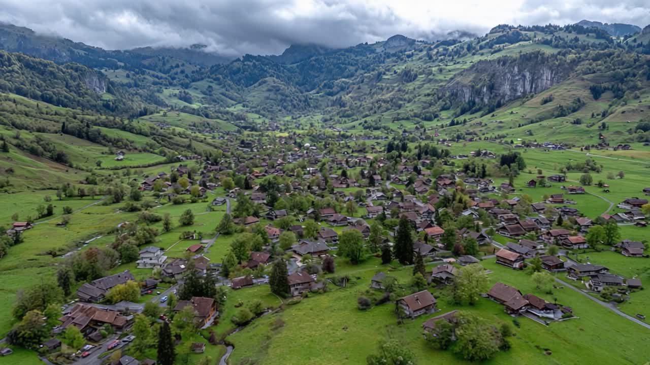 Veduta Aerea di una Pittoresca Valle Montana con Paesaggi Verdi Lussureggianti e un Caratteristico Borgo Costellato di Case Incantevoli Sotto un Cielo Nuvoloso e Drammatico