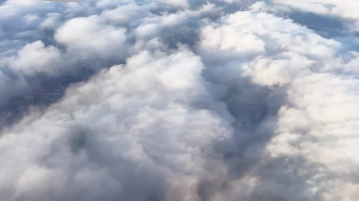 Close aerial view above soft cloud layers, with bright white formations, blue shadows, and dreamy sky texture for travel and weather footage.