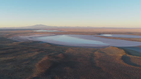 aerial drone view of salinas del diamante basin in mendoza, argentina, reveals vast salt flats surrounded by arid terrain with the andes in the distance under warm evening light
