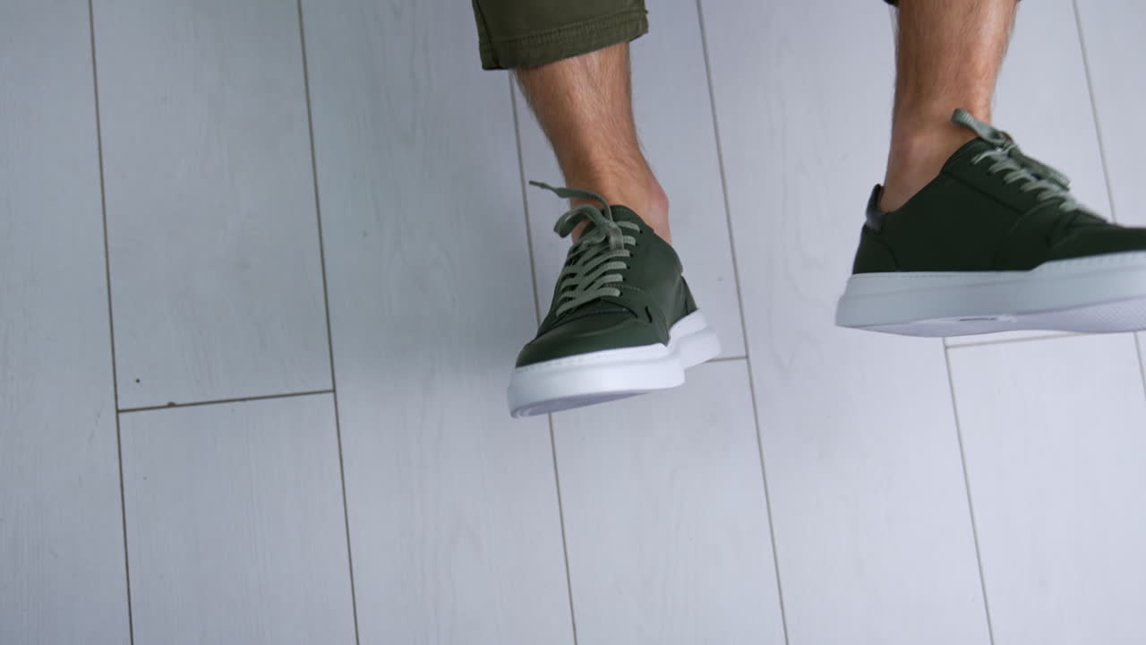 Man's Feet in Green Sneakers on Light Wood Floor