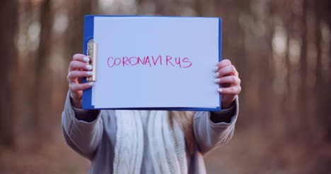 woman with protective mask holding coronavirus inscription in hands in forest 1