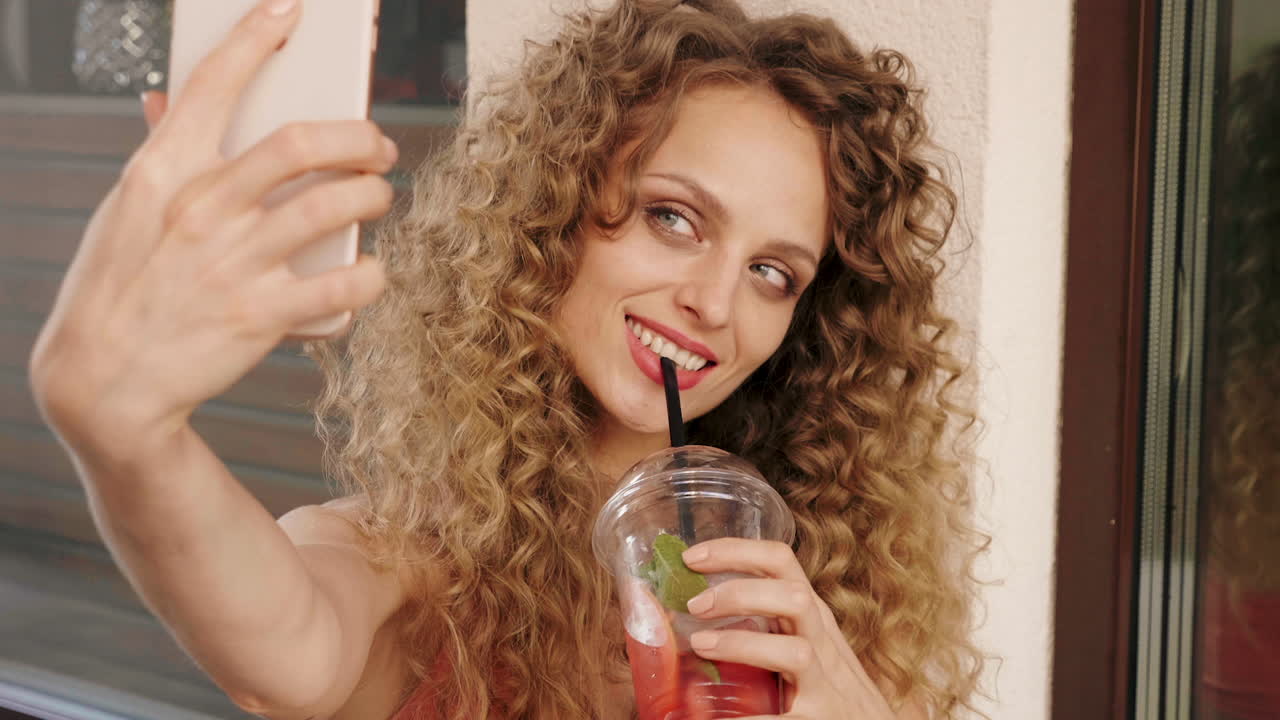 밖에서 상쾌한 음료를 마시면서 셀피를 찍는 여자