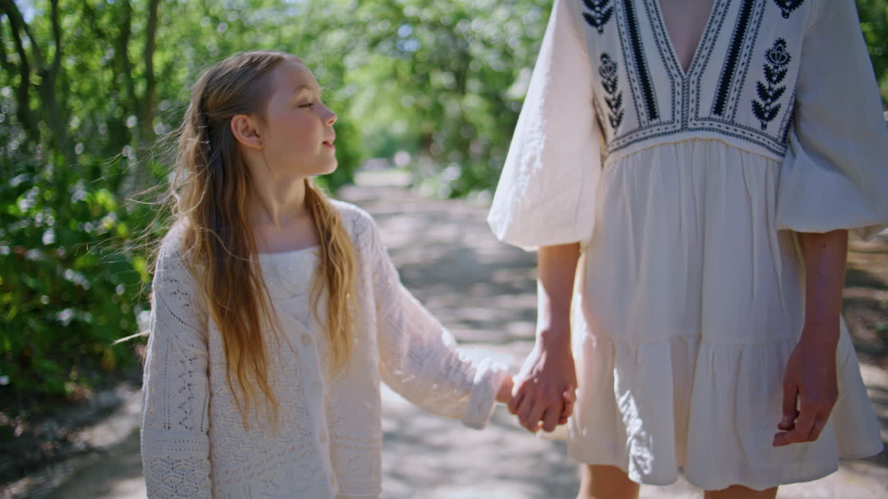Mother leading little daughter by hand walking on green park closeup