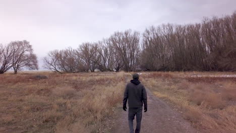 a man walks along a dirt road in an empty field in winter